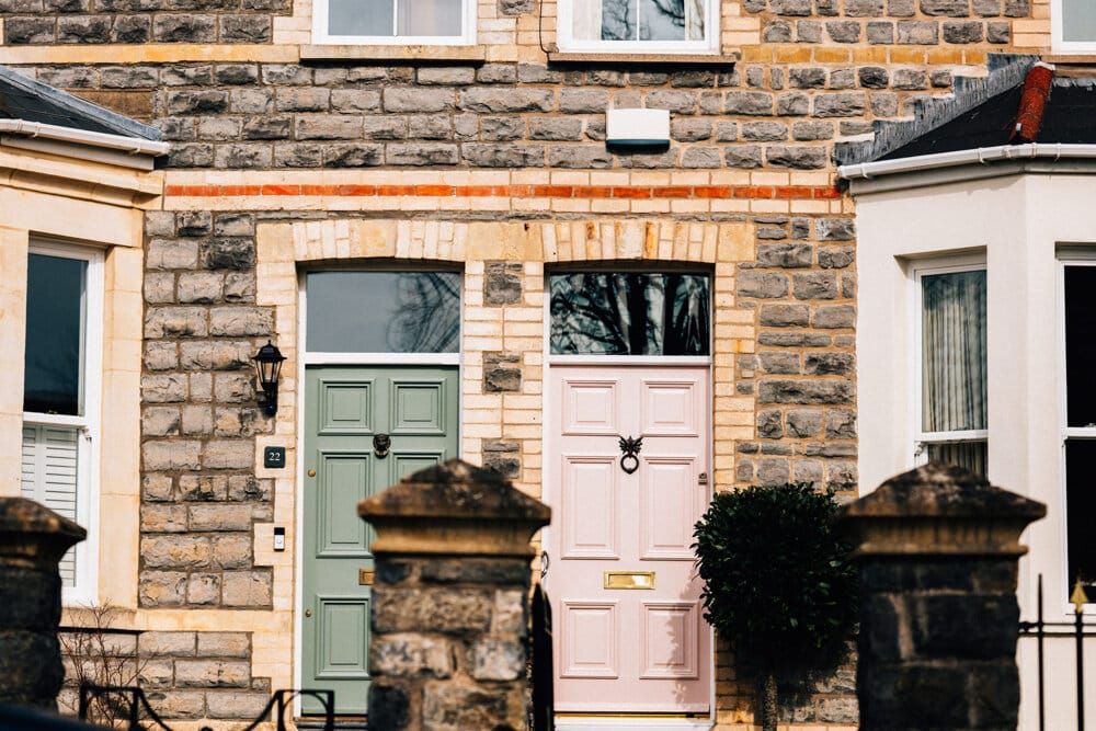Two front doors of a stone terrace, one sage green and one pink
